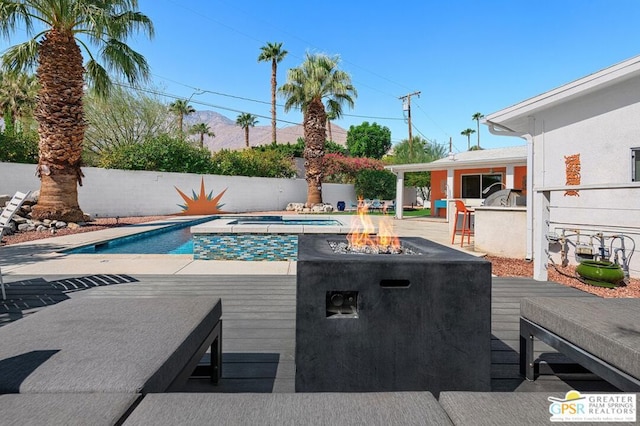 view of swimming pool featuring a wooden deck, an in ground hot tub, exterior kitchen, and an outdoor fire pit