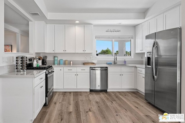 kitchen featuring white cabinets, appliances with stainless steel finishes, light wood-type flooring, and sink