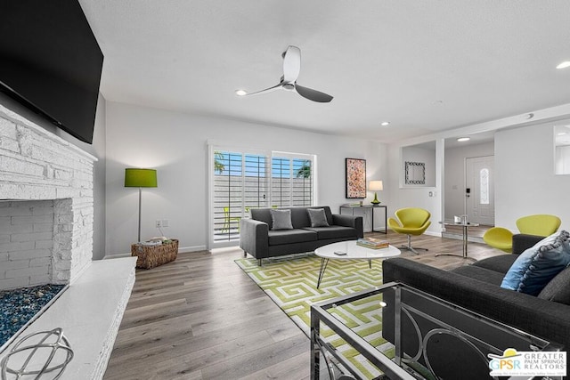 living room with wood-type flooring, a stone fireplace, and ceiling fan