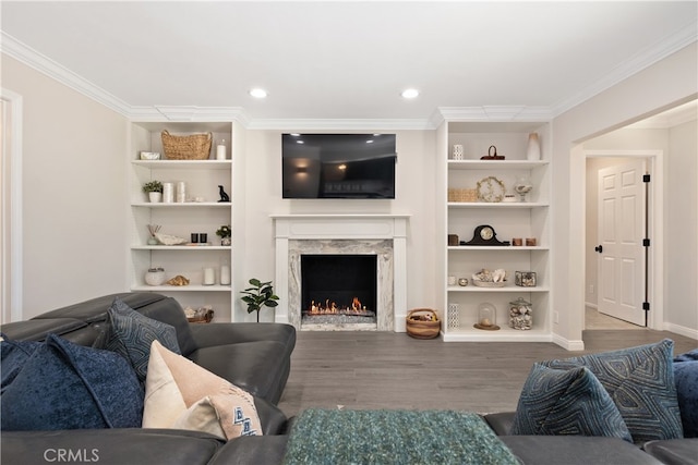 living room with built in features, ornamental molding, wood-type flooring, and a fireplace