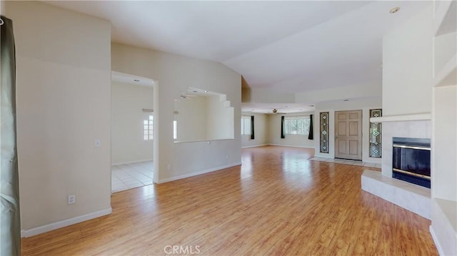 unfurnished living room featuring ceiling fan, lofted ceiling, a fireplace, and light hardwood / wood-style flooring