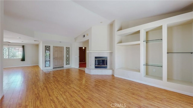 unfurnished living room with built in features, vaulted ceiling, and light wood-type flooring