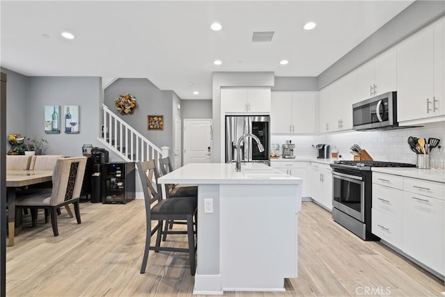 kitchen featuring an island with sink, appliances with stainless steel finishes, light hardwood / wood-style floors, and white cabinetry