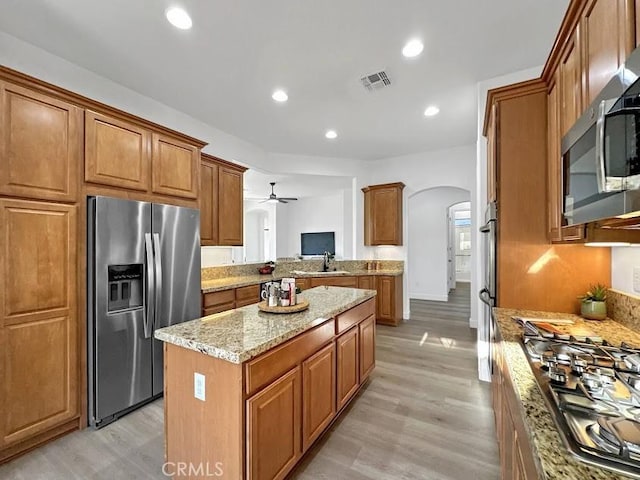 kitchen featuring a center island, sink, light wood-type flooring, light stone counters, and stainless steel appliances