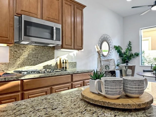 kitchen featuring decorative backsplash, ceiling fan, light stone countertops, and appliances with stainless steel finishes