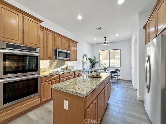 kitchen with light stone countertops, light wood-type flooring, tasteful backsplash, a kitchen island, and stainless steel appliances