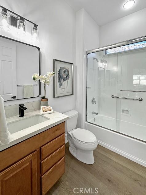 full bathroom featuring vanity, shower / bath combination with glass door, toilet, and wood-type flooring