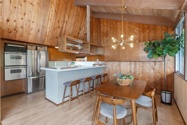 kitchen with wood walls, wood ceiling, stainless steel appliances, and light hardwood / wood-style flooring