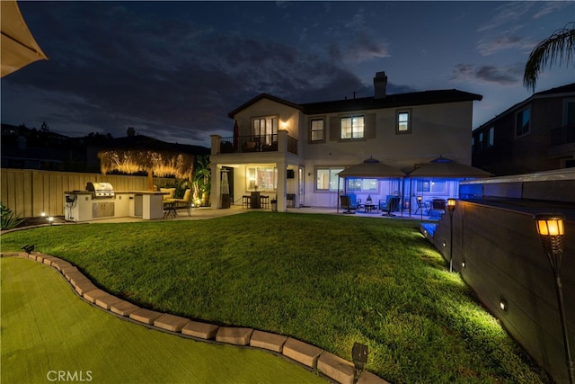 back house at twilight featuring a yard, a balcony, area for grilling, and a patio area