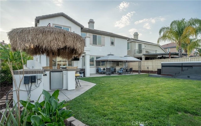 back of property featuring a patio, a yard, an outdoor kitchen, and a hot tub