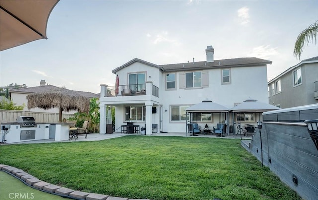 back of property with a balcony, a patio area, and a lawn