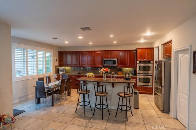 kitchen featuring a kitchen bar, appliances with stainless steel finishes, decorative backsplash, a kitchen island with sink, and decorative light fixtures