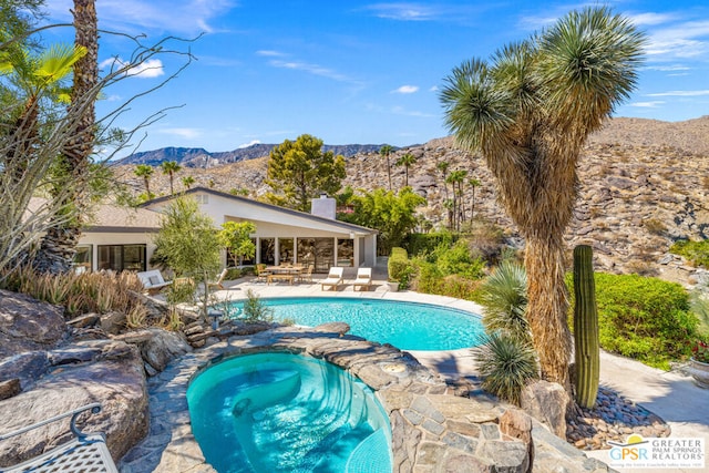 view of pool featuring a patio area, a mountain view, and an in ground hot tub