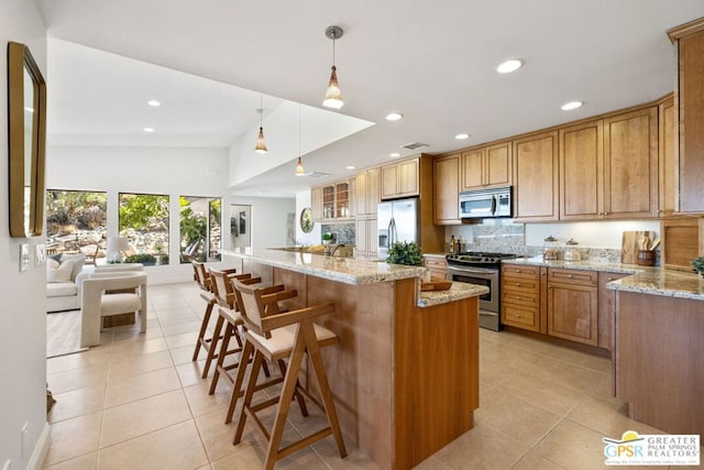 kitchen featuring pendant lighting, stainless steel appliances, an island with sink, backsplash, and a breakfast bar