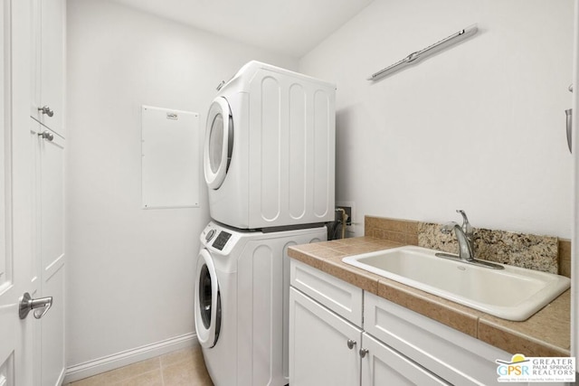 laundry room featuring cabinets, light tile patterned floors, stacked washer and clothes dryer, and sink