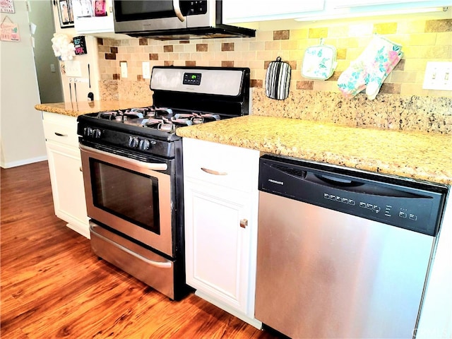 kitchen with tasteful backsplash, white cabinets, appliances with stainless steel finishes, and hardwood / wood-style flooring