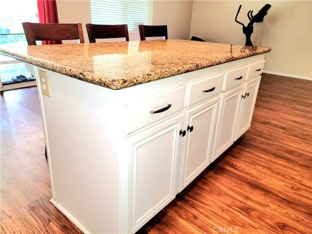 kitchen with light stone countertops, dark hardwood / wood-style floors, a center island, and white cabinetry