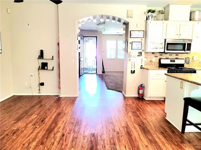 kitchen with white cabinets, black gas stove, dark hardwood / wood-style floors, light stone countertops, and decorative backsplash