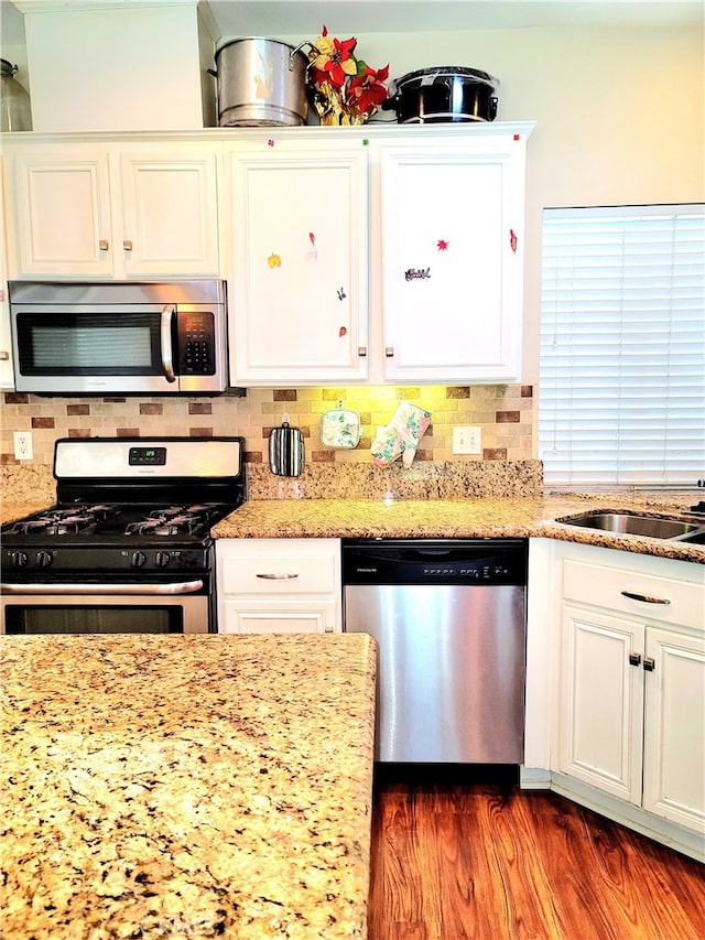 kitchen with dark wood-type flooring, light stone counters, stainless steel appliances, backsplash, and white cabinets