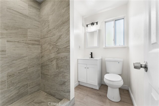 bathroom featuring vanity, toilet, wood-type flooring, and tiled shower