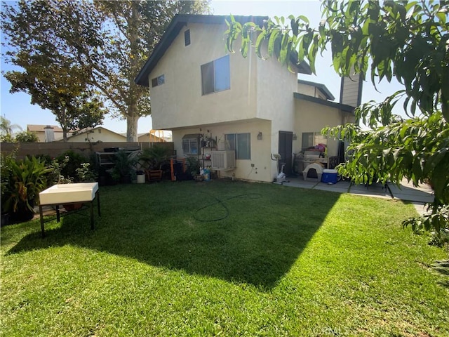 rear view of property with a lawn, fence, and stucco siding