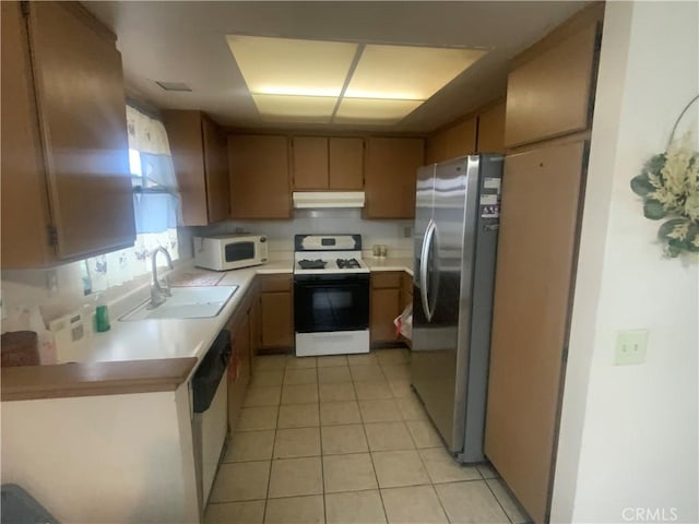 kitchen featuring range with gas cooktop, white microwave, freestanding refrigerator, light countertops, and a sink