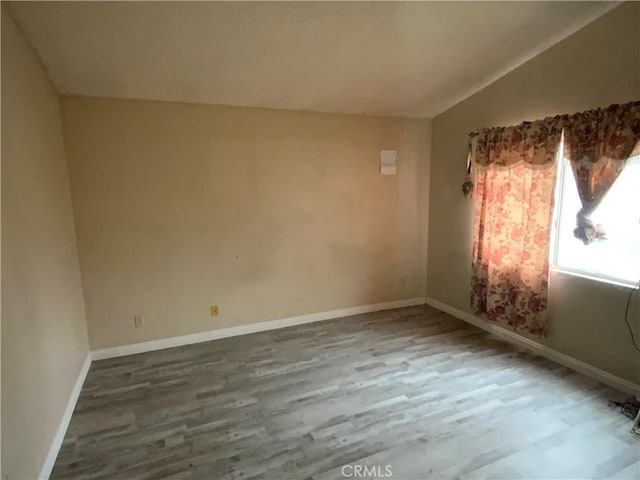 unfurnished room with baseboards, vaulted ceiling, and wood finished floors