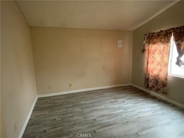 spare room featuring vaulted ceiling, baseboards, and wood finished floors