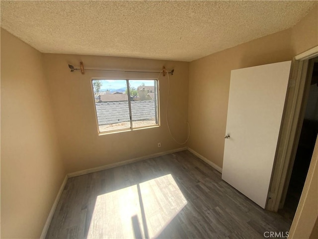 unfurnished room with a textured ceiling, baseboards, and dark wood-type flooring