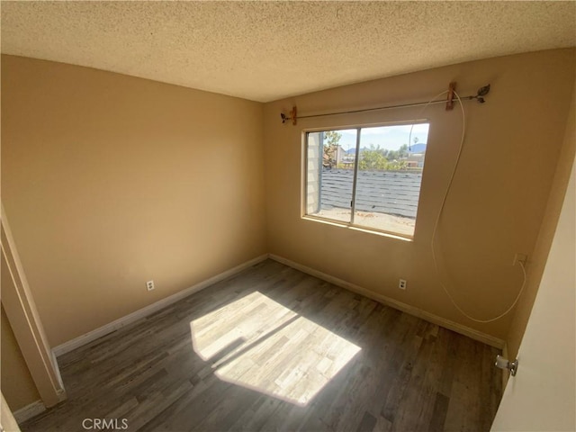 unfurnished room featuring a textured ceiling, dark wood finished floors, and baseboards