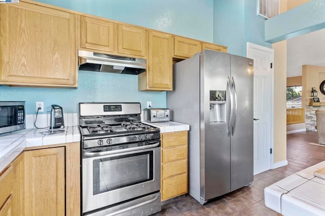 kitchen with tile counters, dark wood-type flooring, light brown cabinets, and stainless steel appliances