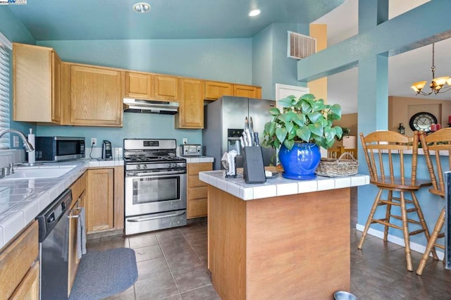 kitchen with appliances with stainless steel finishes, tile counters, a center island, and vaulted ceiling