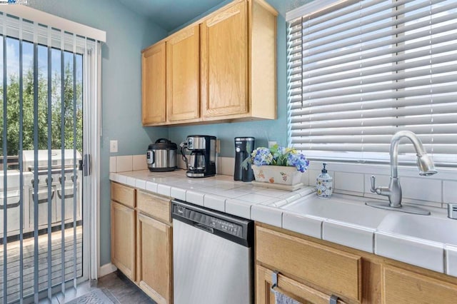 kitchen featuring light brown cabinets, light tile patterned floors, sink, stainless steel dishwasher, and tile counters