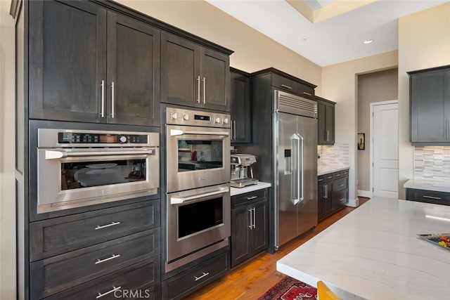 kitchen featuring light stone counters, light hardwood / wood-style flooring, appliances with stainless steel finishes, and decorative backsplash