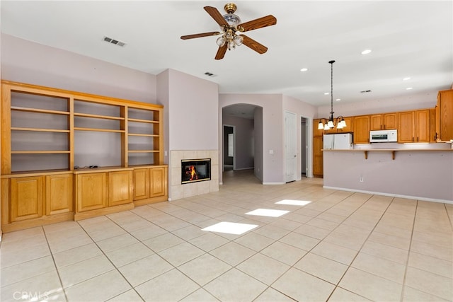 unfurnished living room with ceiling fan with notable chandelier, a fireplace, and light tile patterned flooring