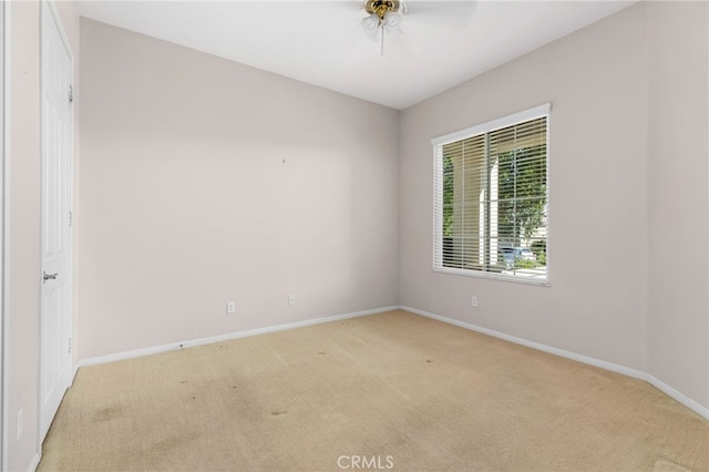 spare room with light colored carpet, baseboards, and a ceiling fan