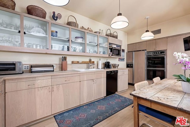 kitchen featuring light brown cabinets, black appliances, sink, hanging light fixtures, and light hardwood / wood-style flooring