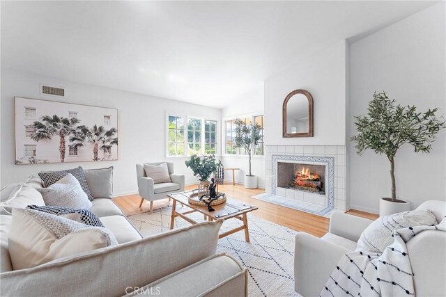 living area with vaulted ceiling, visible vents, a fireplace, and wood finished floors