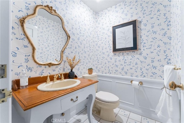 bathroom featuring vanity, wallpapered walls, wainscoting, a decorative wall, and toilet