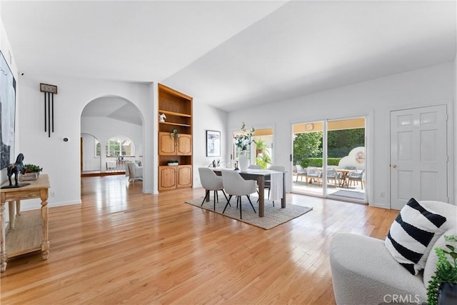 dining space with arched walkways, light wood finished floors, lofted ceiling, and a wealth of natural light