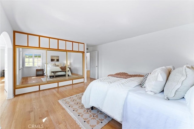 bedroom with light wood-type flooring and arched walkways