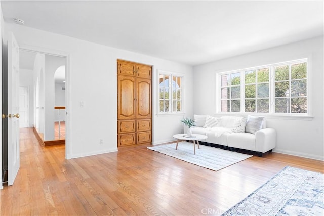 unfurnished living room with baseboards, arched walkways, and light wood finished floors