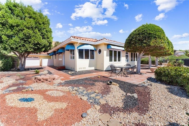 back of house with a patio area, stucco siding, a tiled roof, and a garage