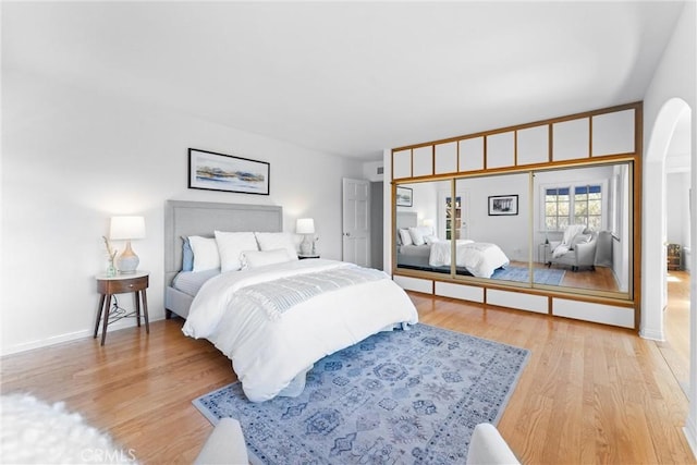 bedroom featuring baseboards, arched walkways, and light wood-style flooring