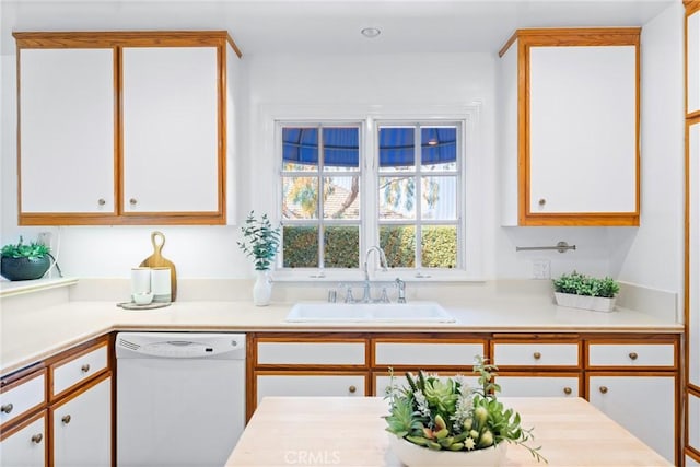 kitchen with white cabinets, dishwasher, light countertops, and a sink