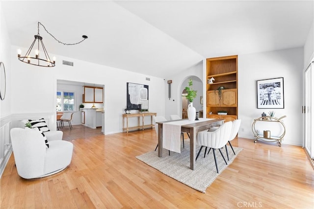 dining area with light hardwood / wood-style floors, built in features, a notable chandelier, and vaulted ceiling