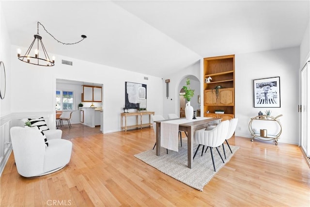 dining room featuring light wood-type flooring, visible vents, arched walkways, and an inviting chandelier