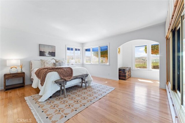 bedroom with arched walkways, baseboards, and light wood-style floors