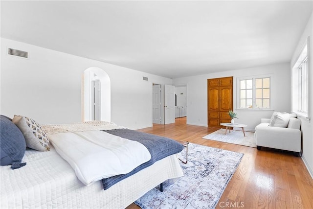 bedroom featuring visible vents, arched walkways, light wood-style floors, and baseboards