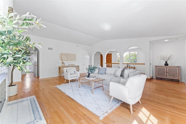 living room with light wood-type flooring, arched walkways, lofted ceiling, and visible vents